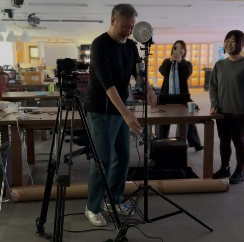 映像作家鈴木佑介が照明機材を使っている。その姿を写真に撮る女性。