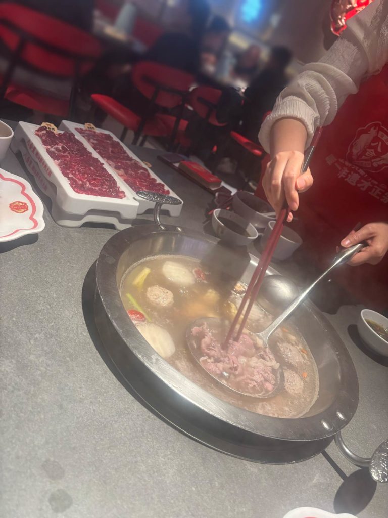 火鍋の鍋に牛肉と野菜を入れて、箸で取り出そうとしている場面