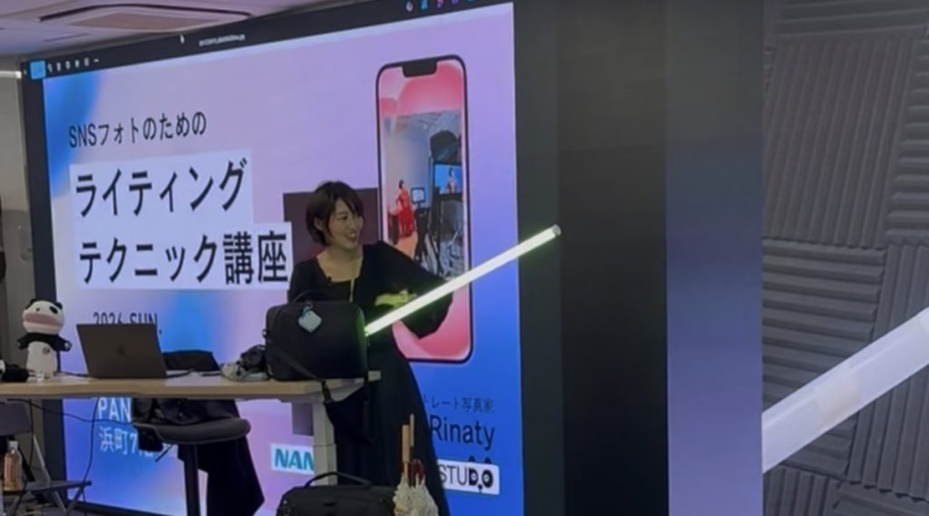 棒状のライトを手に持って写真作品の撮り方をレクチャーする女性の写真家