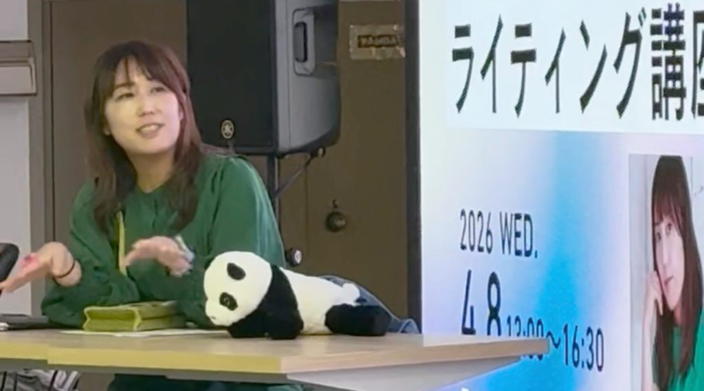 写真家の女性がテーブルの前にして登壇している。手前にはパンダのぬいぐるみ。