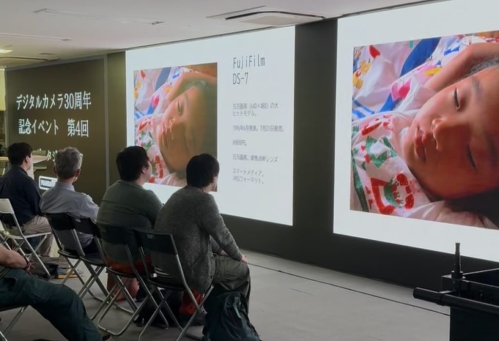 昔のデジカメで撮った画像がモニターに映し出されていて観客一同がそれを見ている。