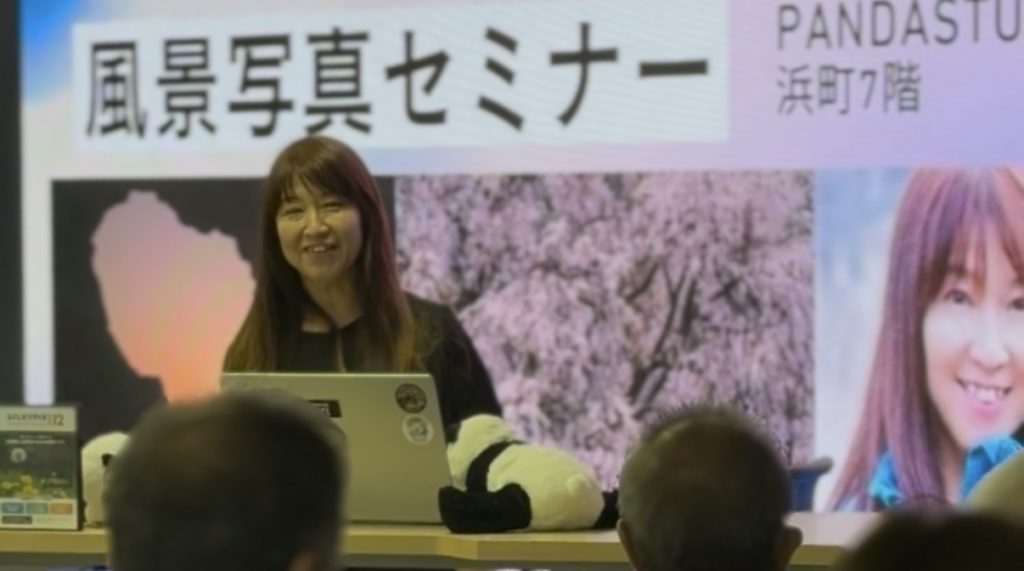 風景写真家井上嘉代子先生がモニターの前で登壇している様子。