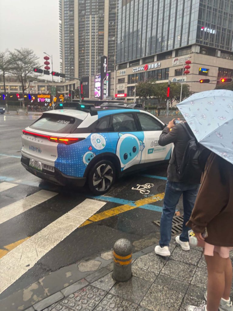 深圳の都市風景。高層ビル群と、街中の赤い信号機が見える。手前に自動運転タクシーが駐車されている