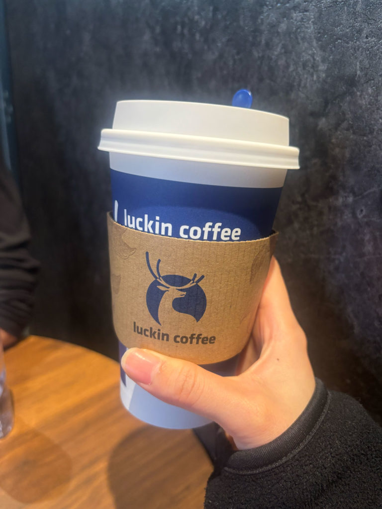 Luckin coffeeのロゴが入った青と白のコーヒーカップ。白いリッド(蓋)が乗っており、暗い背景に照らされている