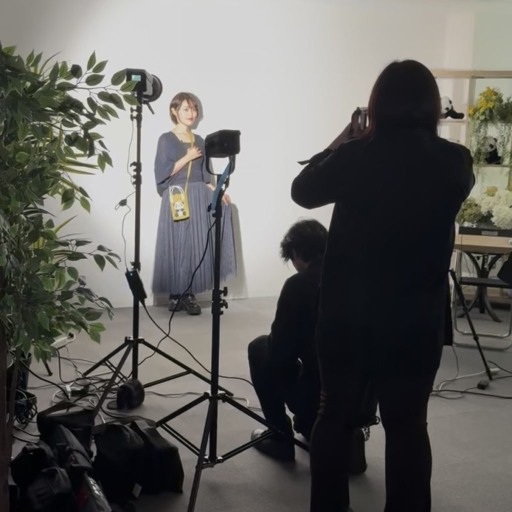 女性の写真家がライトの前でモデルをしている。それを２人がカメラに撮っている。