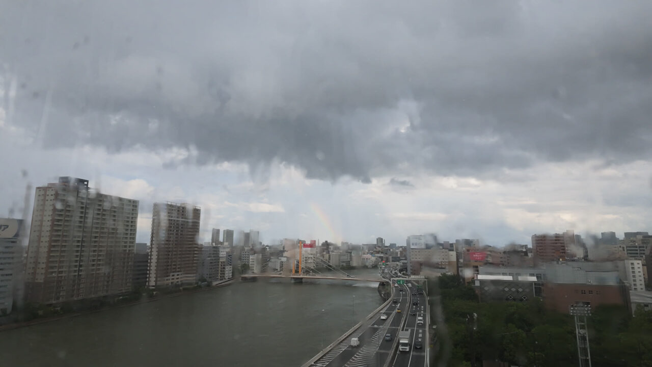 ゲリラ豪雨の最中の隅田川。窓ガラスの水滴で画面がにじんでいるが、雨の向こうにすでに虹がうっすら出ている
