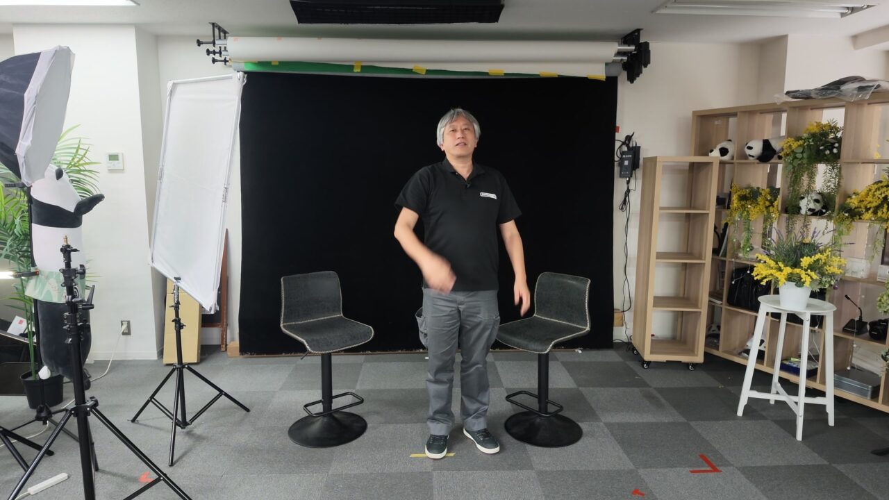 黒背景の前でDJI Mic 3の送信機を胸に付けて話す様子。Osmo Pocket 4Pは2〜3m離れた三脚の上