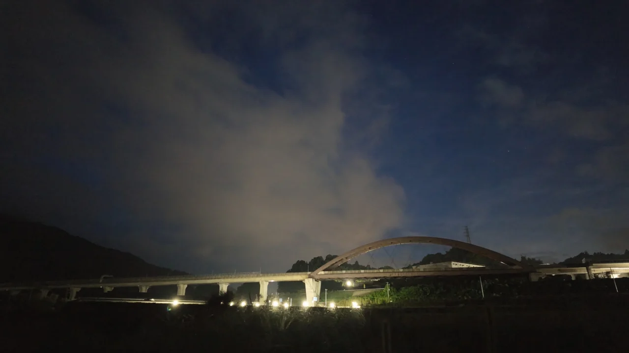 18時40分。低照度モードで撮った夜空。青い空に薄雲が流れ、下にライトアップされたアーチ橋。空の右側に小さな星がいくつか写っている