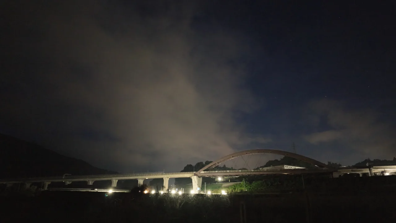 18時45分。低照度モードで撮った夜空。薄雲が斜めに流れ、雲の切れ間に星。アーチ橋の街灯が手前を照らしている